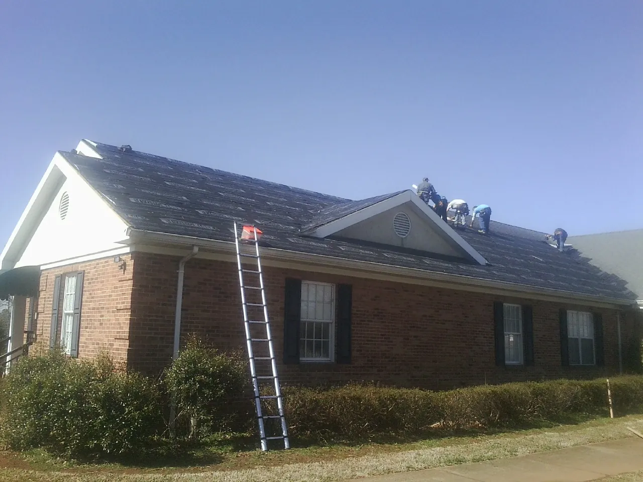 Crew tearing shingles off a brick ranch roof with a ladder set — Metal Roof Repair work by our crew in Dumfries