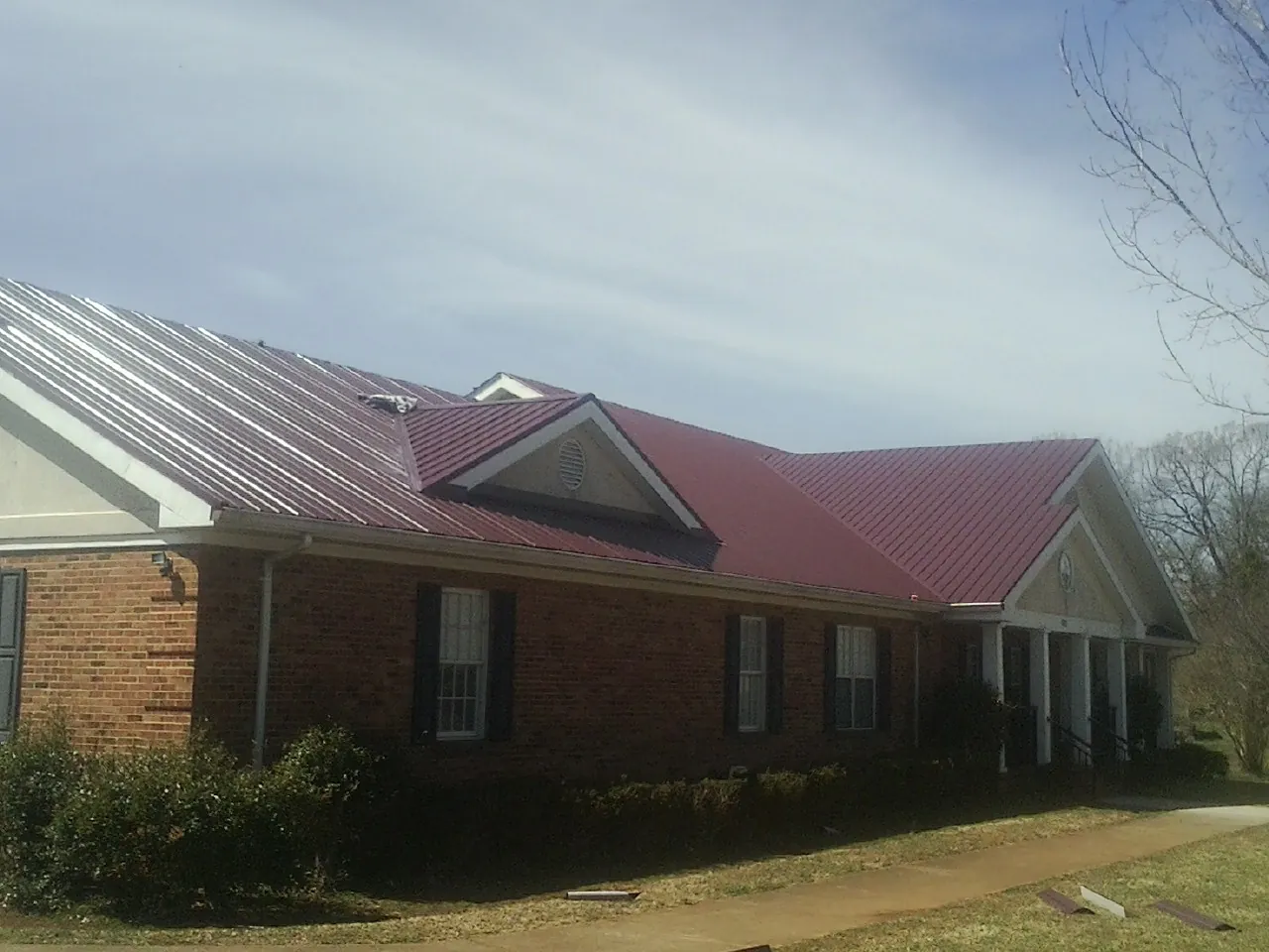 Red metal roof with gabled entries on a long brick building, from a Hail Damage Roof Repair job in Dumfries