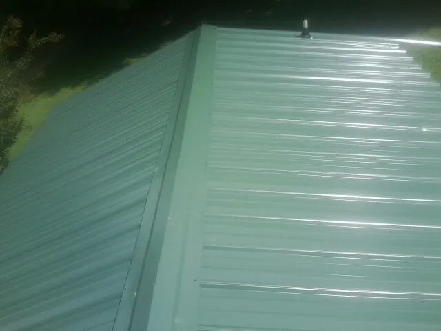 New green metal panels meeting at the ridge of a roof — Flat Roof Repair work by our crew in Dumfries