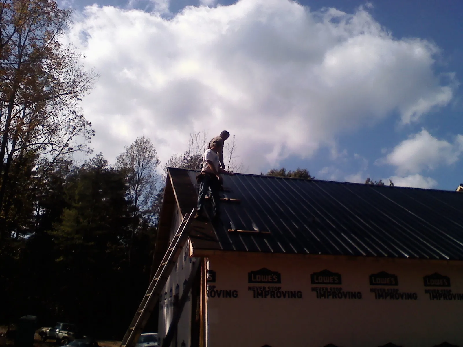Roofer fastening dark metal panels high against a cloudy sky, from a Roof Inspection job in Dumfries